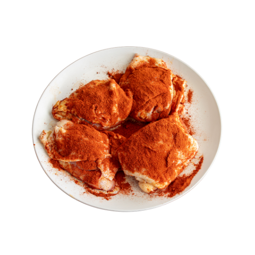 Uncooked chicken thighs seasoned with paprika on a white plate