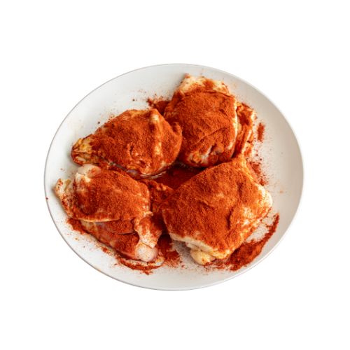 Uncooked chicken thighs seasoned with paprika on a white plate